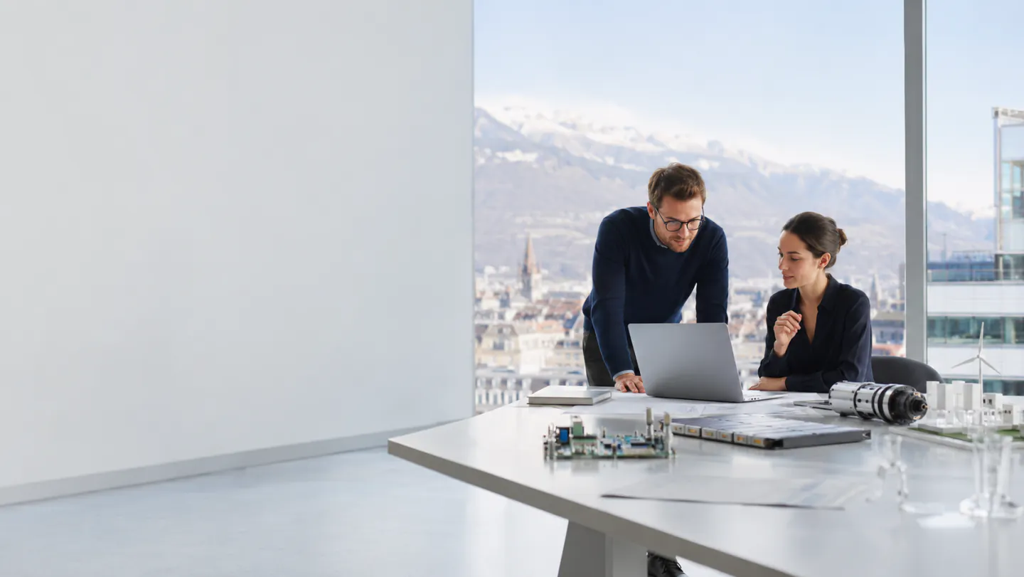 Bureau grenoblois avec vue sur la ville et les massifs enneigés, plans techniques et maquettes sur la table
